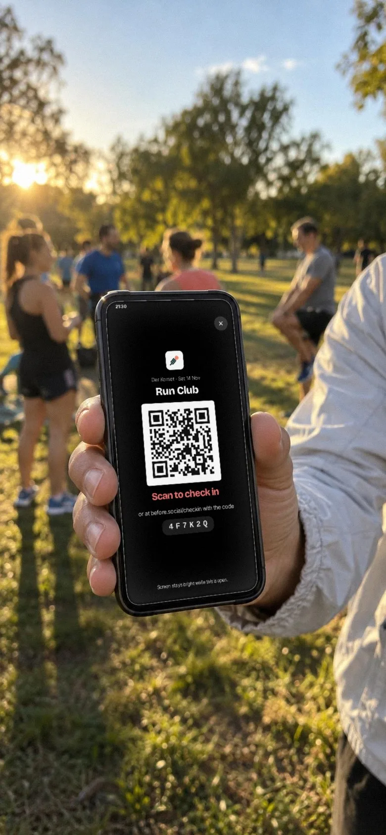 View through a phone camera: a hand holds out a phone with the QR code full screen, the run club in the park behind it