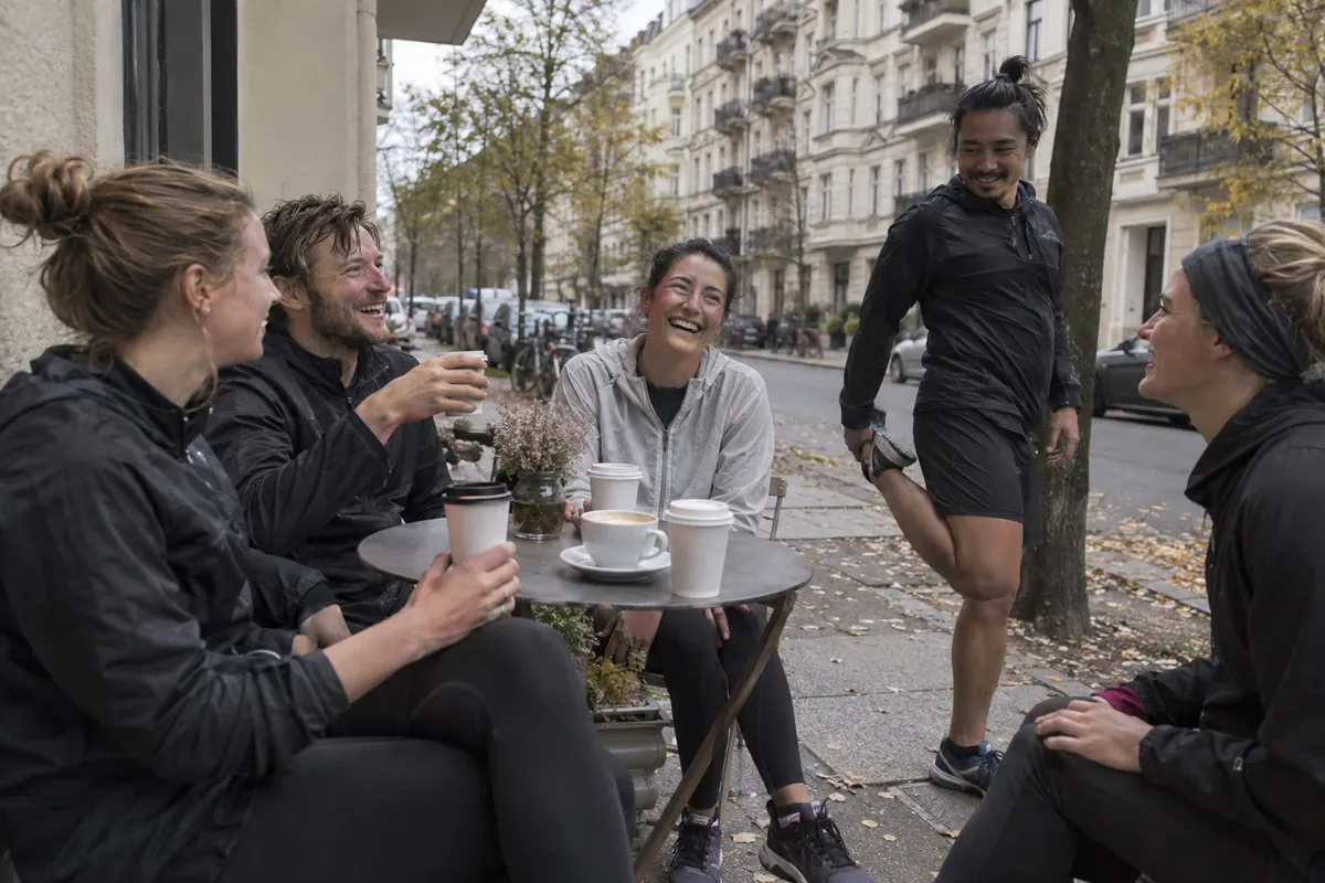 Runners laughing over coffee at a café table on a Berlin pavement after a run