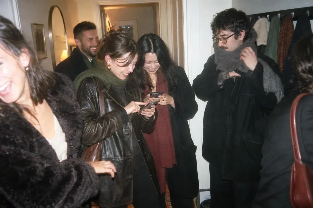 Des invités enfilent leurs vestes près des manteaux à la fin d'un supper club, deux femmes rient en tapant leurs numéros dans un téléphone